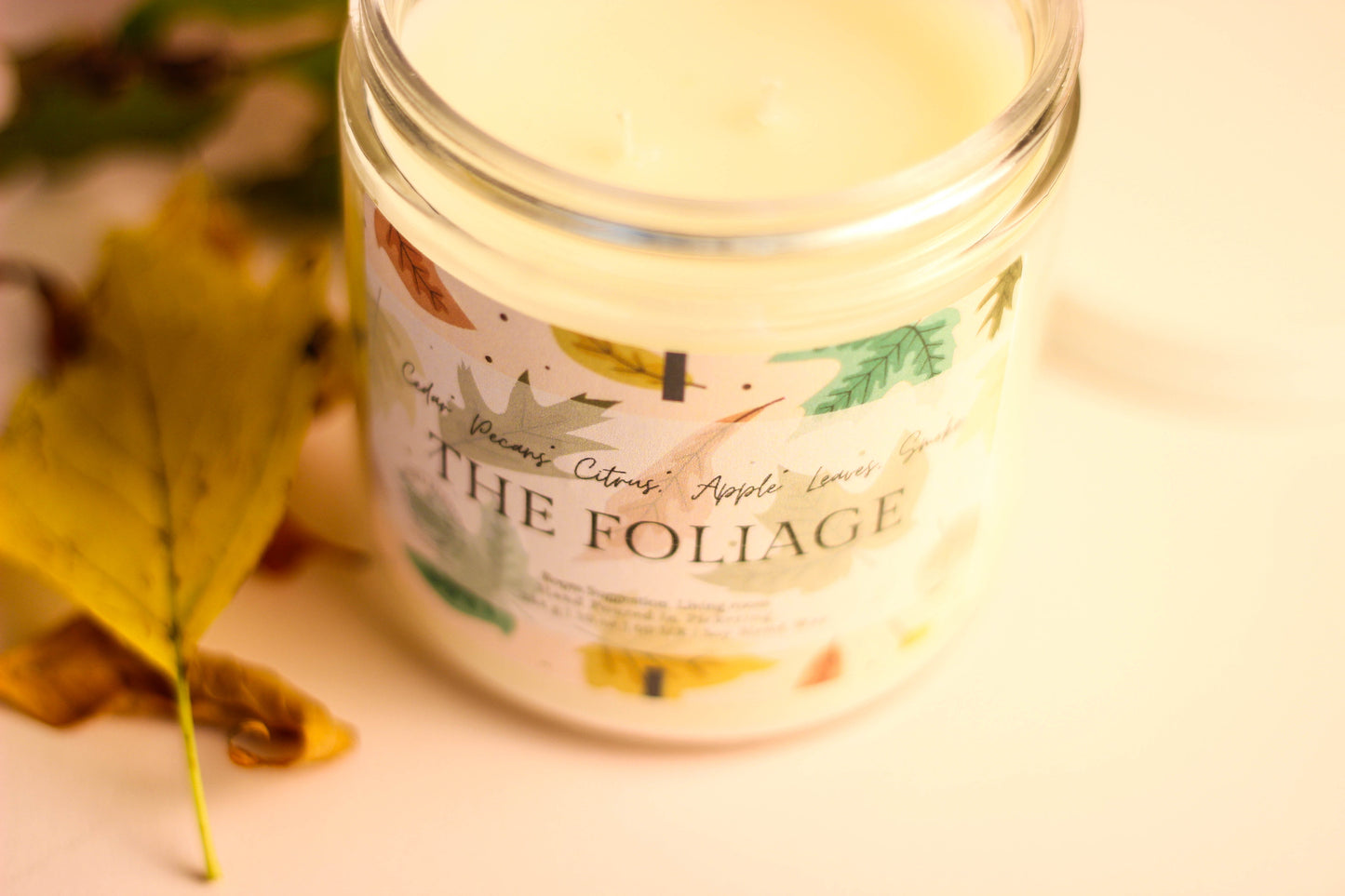 Candle jar labeled 'The Foliage' with autumn leaves on a light background
