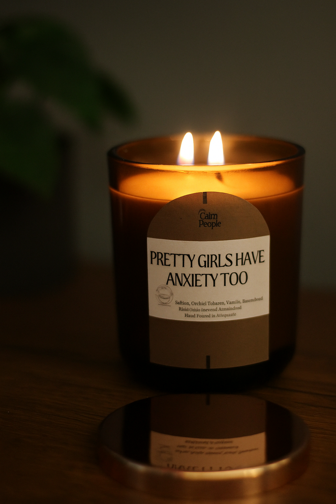 Candle with a label reading 'Pretty Girls Have Anxiety Too' in a dimly lit setting.