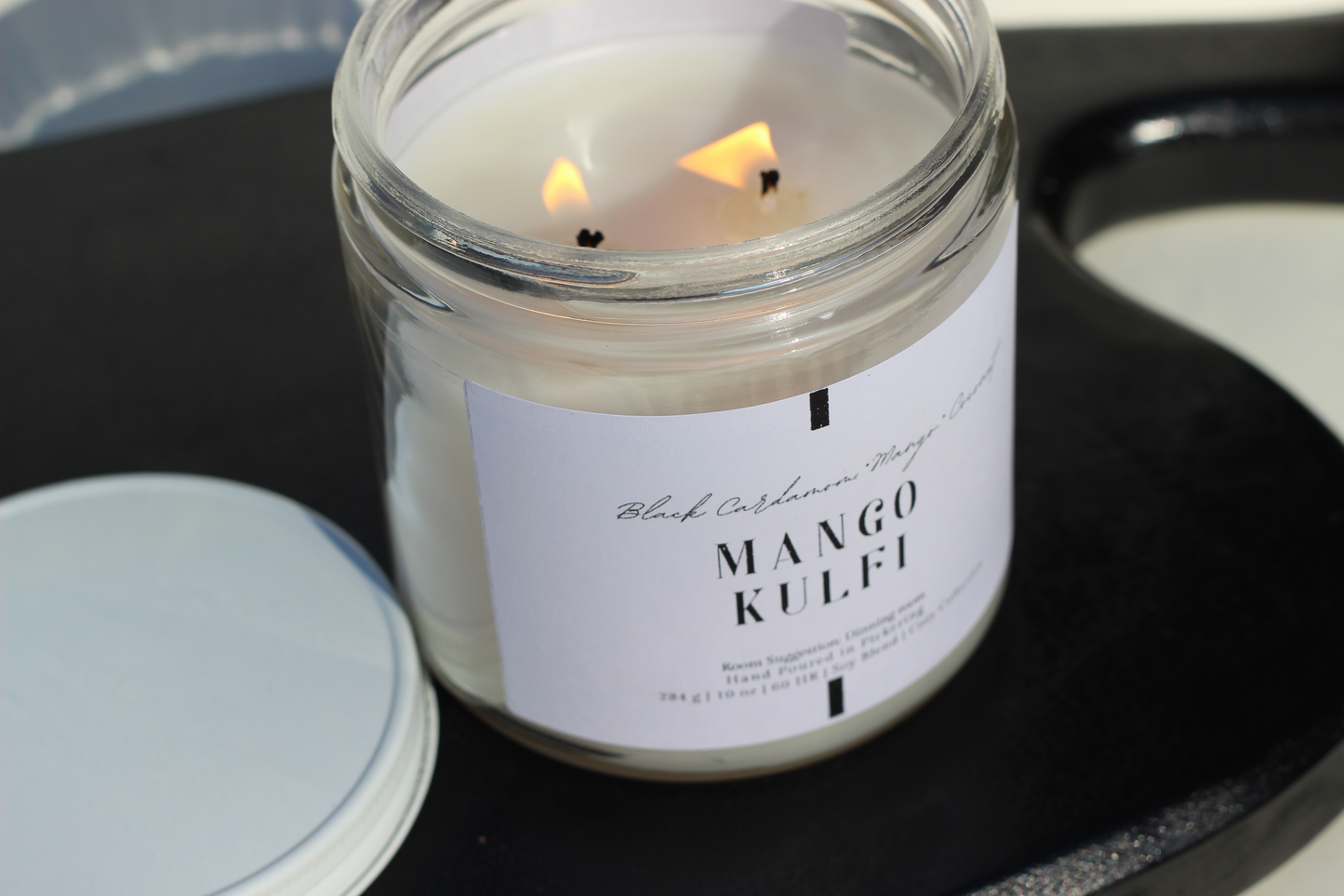Candle in a jar labeled 'Mango Kulfi' on a dark surface