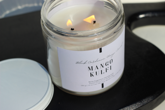 Candle in a jar labeled 'Mango Kulfi' on a dark surface